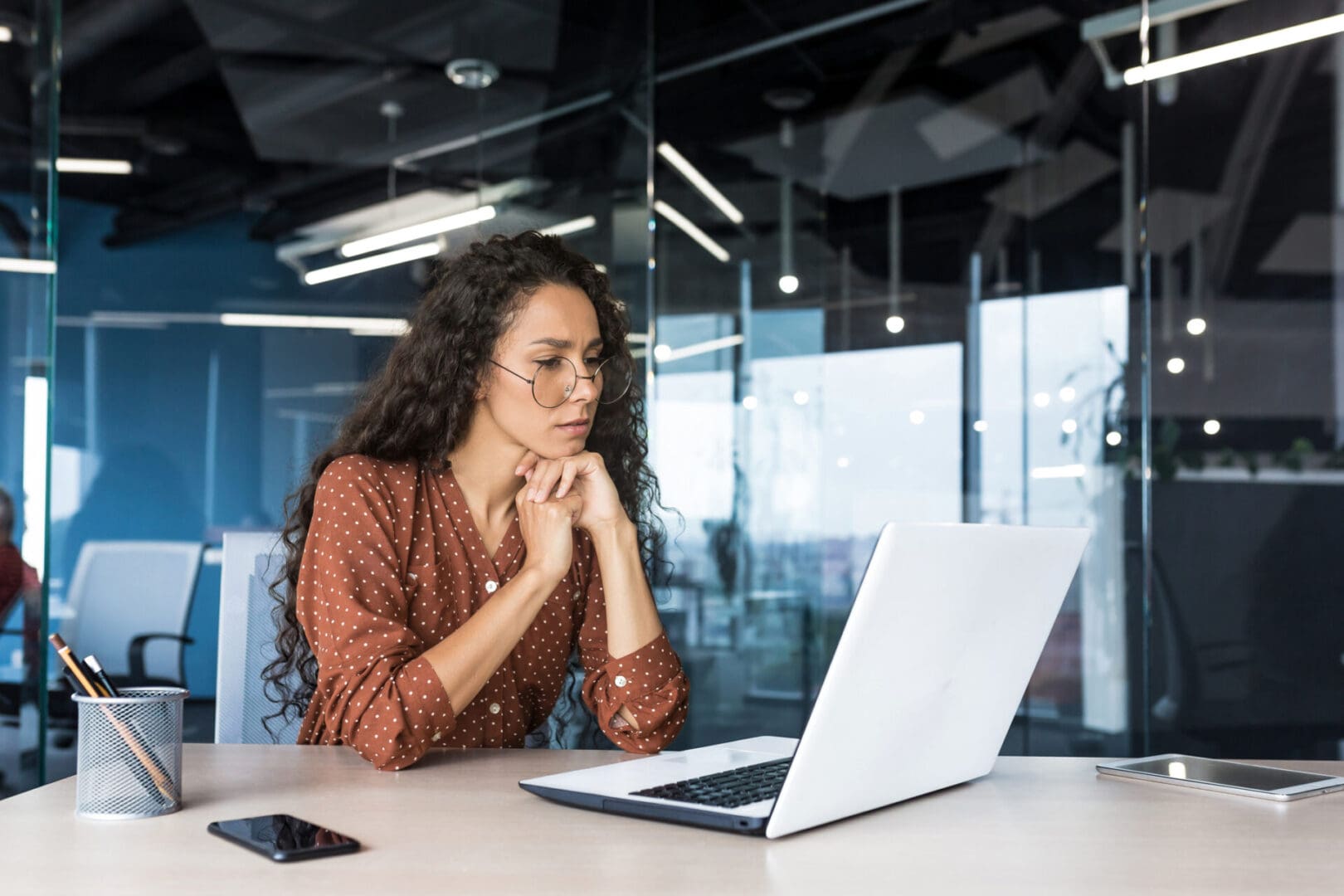 Pensive and focused female programmer web developer working in modern product development company Hispanic woman sitting and thinking using laptop to write code Person focused on laptop in modern office.
