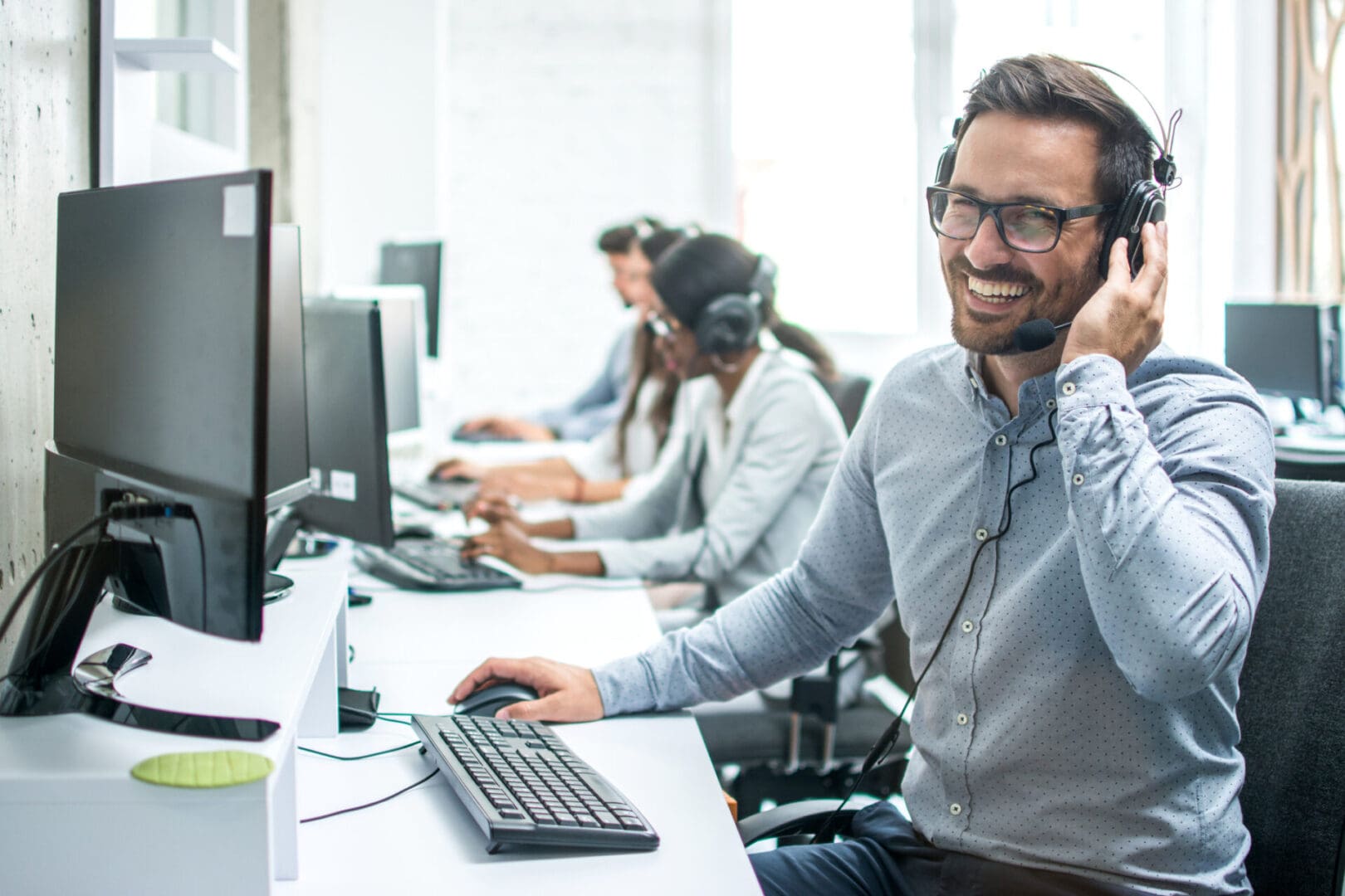 Smiling handsome customer support operator with headset working in call center. Man smiling while working at computer desk.